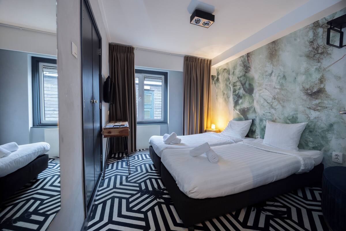 A hotel room with a large bed, a smaller bed, a desk, and a wardrobe.