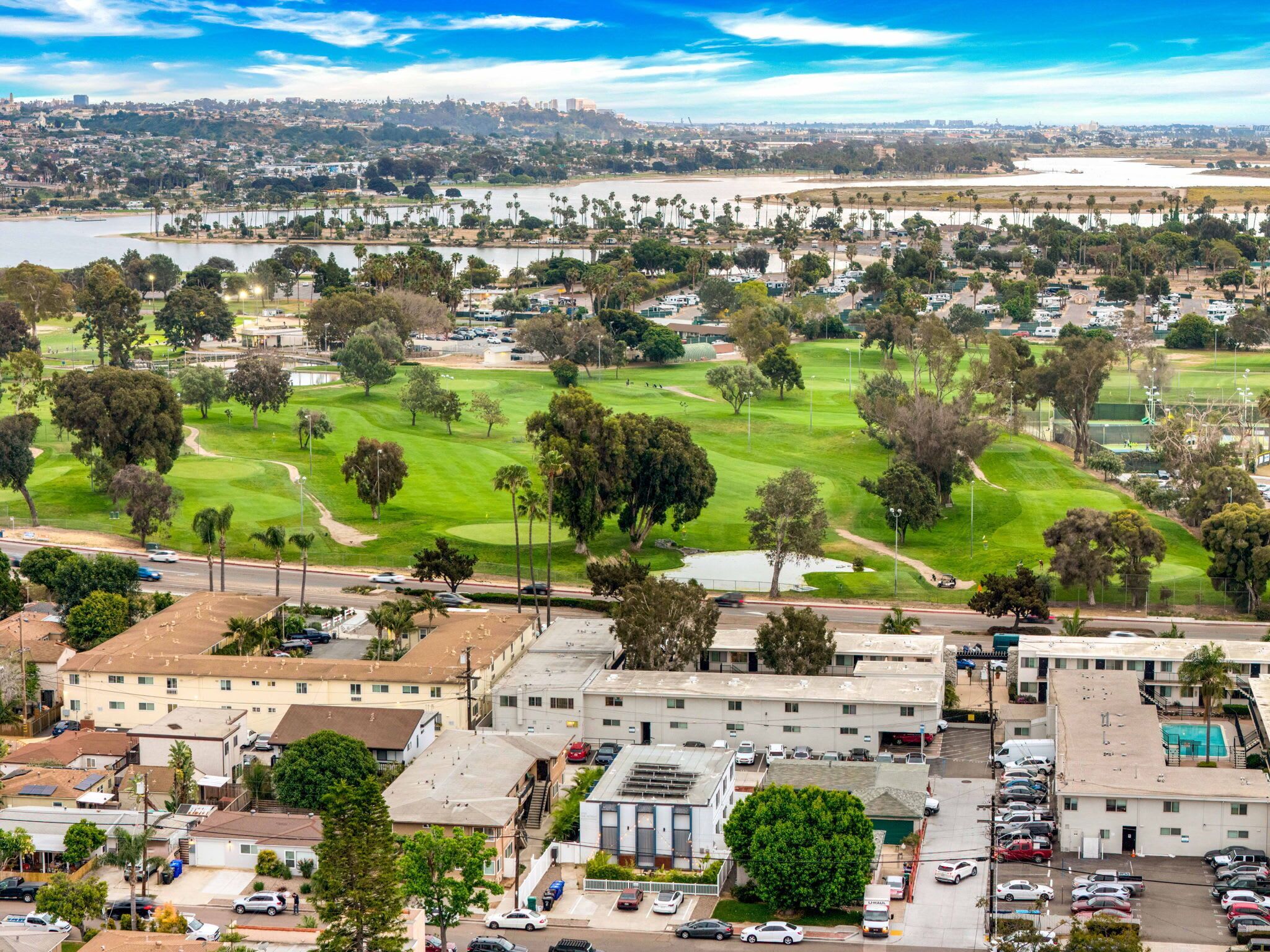 A residential area with a golf course, buildings, and a body of water in the background.