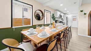 Un coin repas avec une longue table en bois, dressée pour six personnes, entourée de chaises en osier.