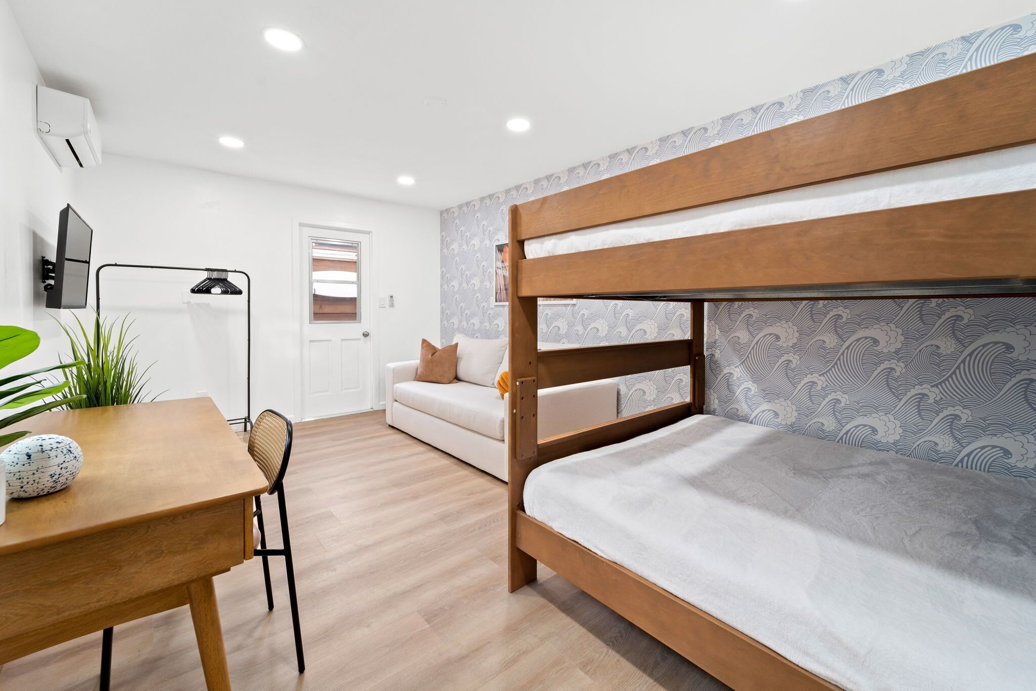 Una habitación moderna con una cama litera, un sofá, una mesa de comedor y una planta en maceta.