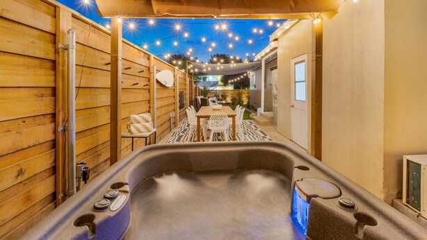 Un espace avec un bain à remous, des murs en bois, une table, des chaises et des guirlandes lumineuses suspendues au-dessus.
