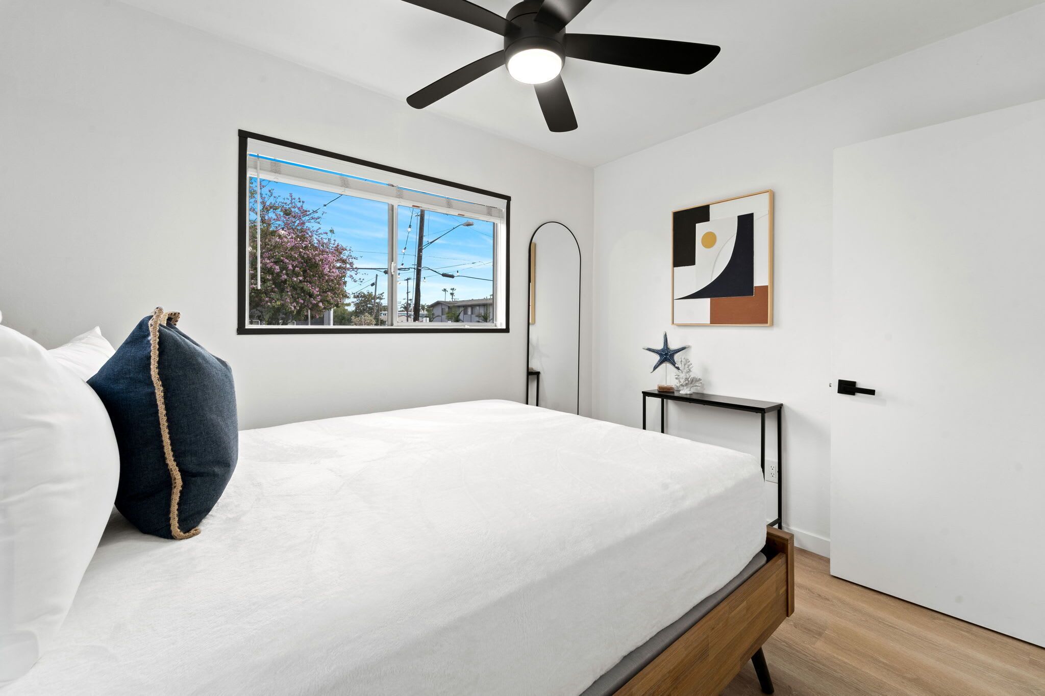 A bedroom with a bed, a ceiling fan, a window with a view, and a door.