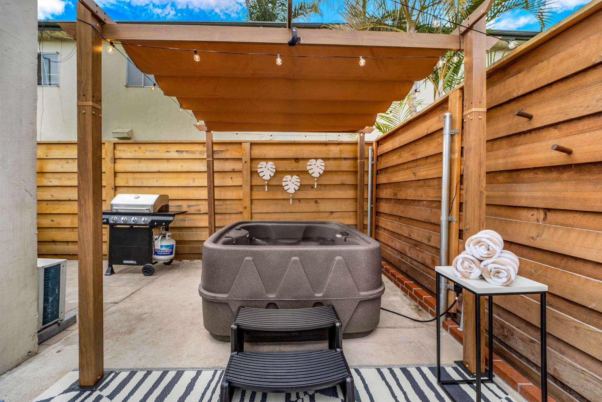 Una terraza de madera con un jacuzzi, una parrilla y una mesa con toallas.