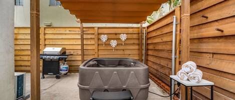 Una terraza de madera con un jacuzzi, una parrilla y una mesa con toallas.