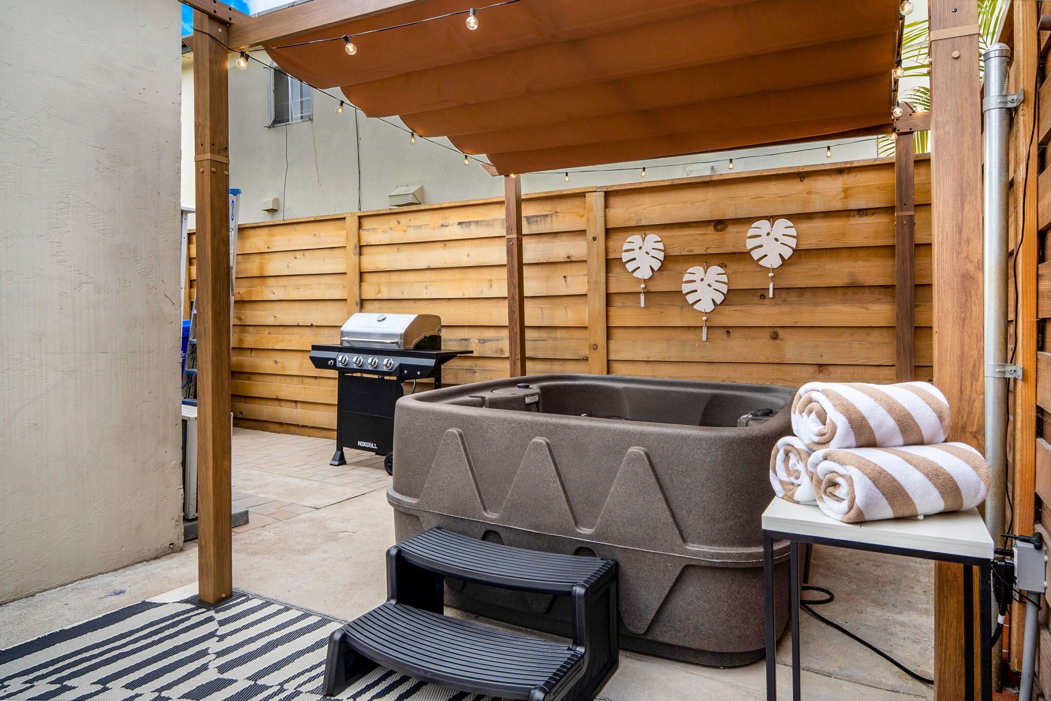 A backyard with a hot tub, a barbecue grill, and a wooden fence.