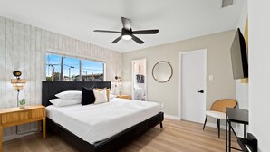 Une chambre à coucher moderne, comprenant un lit, des tables de chevet, un ventilateur de plafond, une fenêtre et une porte.
