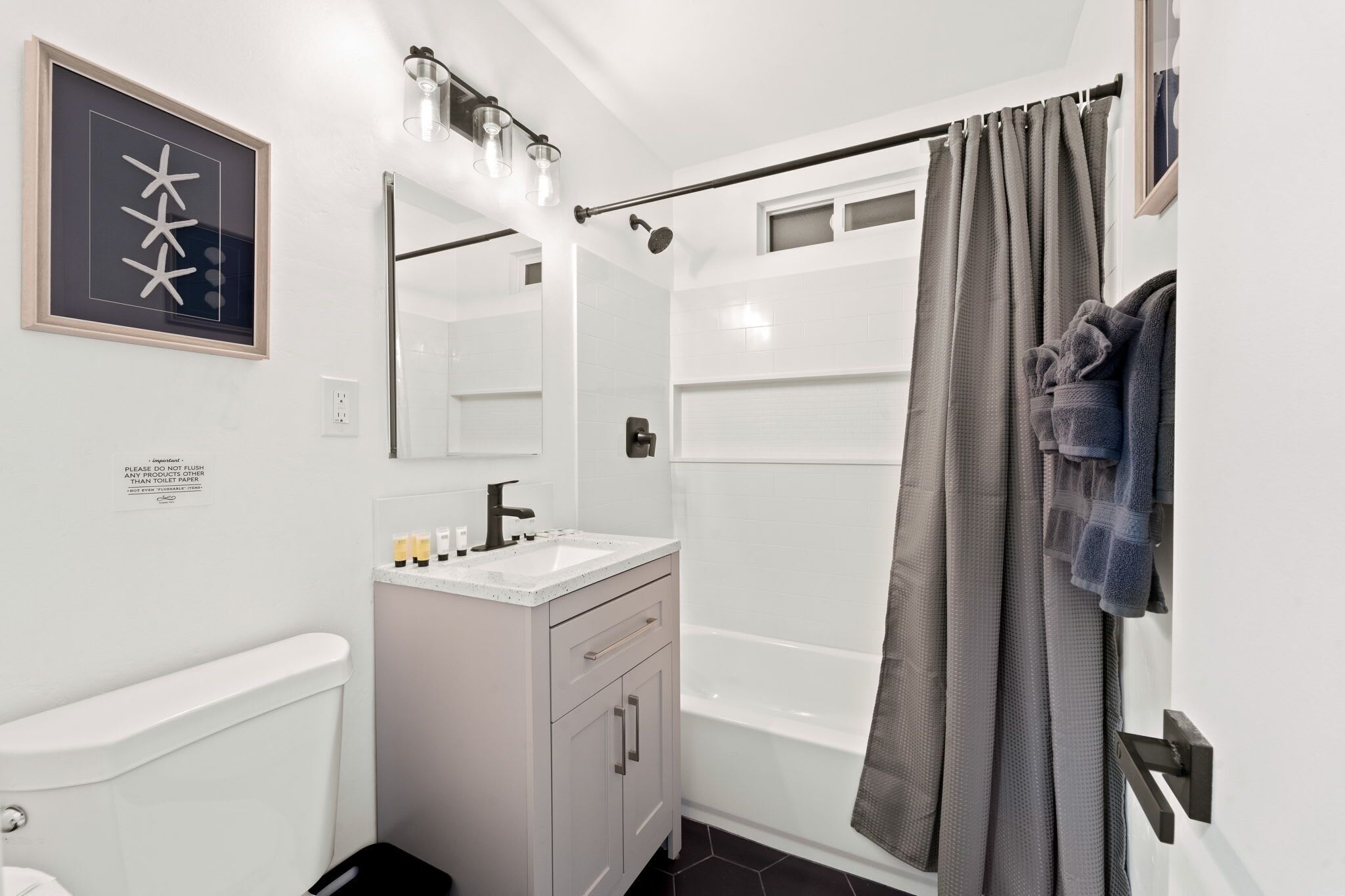 A modern bathroom with a white vanity, a large mirror, a shower curtain, and a framed artwork on the wall.