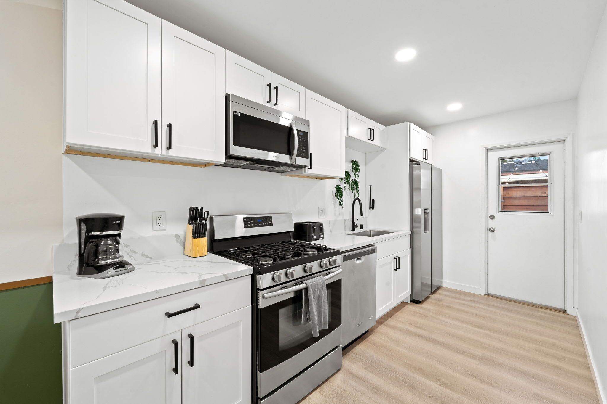 A modern kitchen with white cabinets, stainless steel appliances, and a wooden floor.