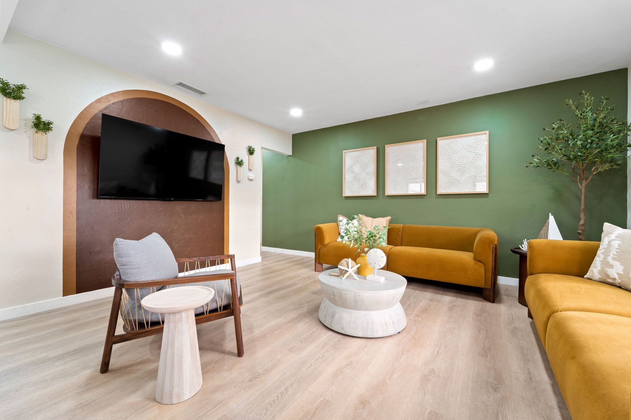 A modern living room with a sofa, armchair, and coffee table, a flat-screen TV mounted on a wall, and decorative wall art.