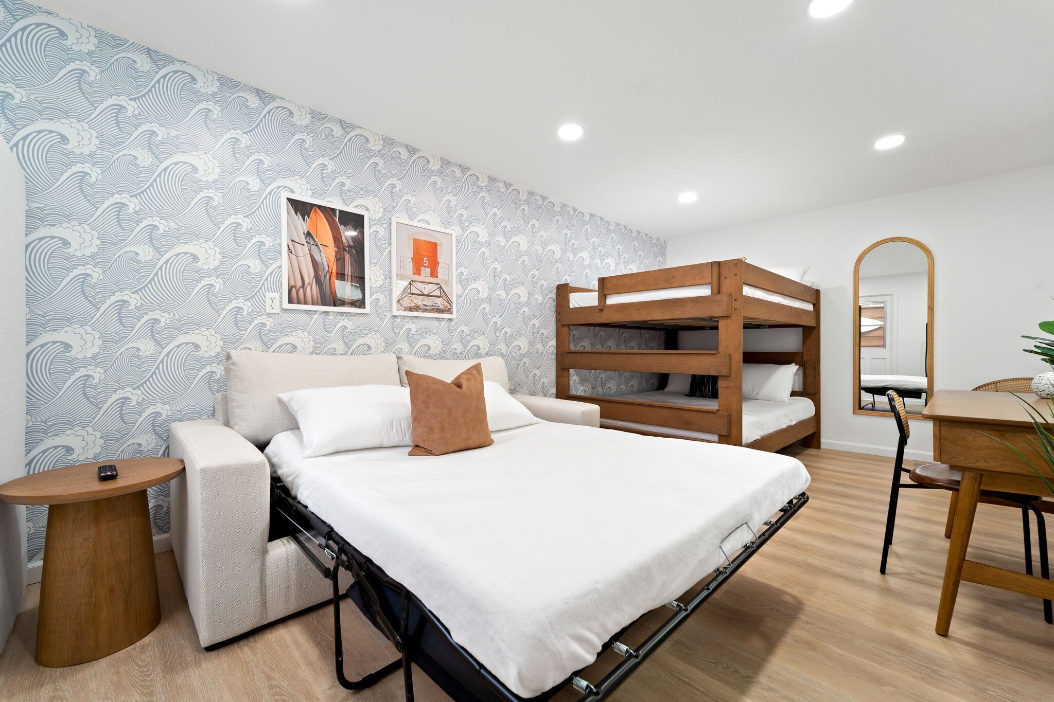 Un dormitorio moderno con una cama litera, un sofá, una mesita y un espejo.