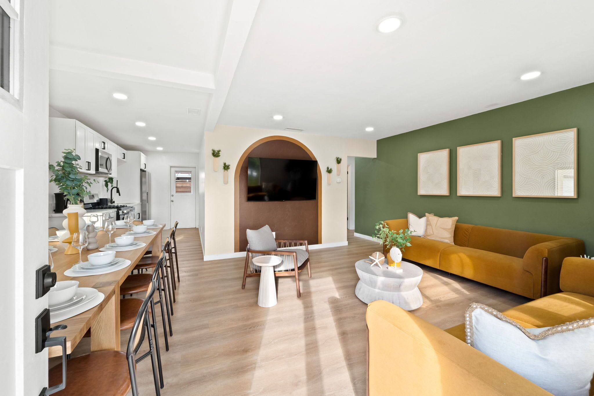 Un salon moderne avec un canapé, une table à manger dressée pour quatre personnes et un coin cuisine visible à travers une arche.