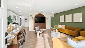 Un salon moderne avec un canapé, une table à manger dressée pour quatre personnes et un coin cuisine visible à travers une arche.