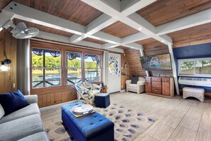 A spacious living area with a large window, a ceiling fan, a sofa, a coffee table, a TV, and a cabinet. - Sunrise Oasis – Lakefront Living (Sunrise Beach)