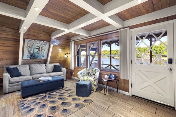 A room with a wooden ceiling, a sofa, a patterned armchair, a door with a diamond pattern, and a view of greenery outside. - Sunrise Oasis – Lakefront Living (Sunrise Beach)