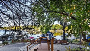 Un escalier en bois mène à une zone de quai où se trouve une petite cabane bleue, au bord d’un lac paisible.