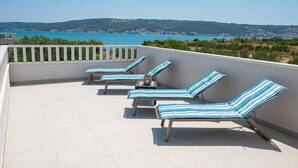 A terrace with four striped lounge chairs, a white balustrade, and a view of a coastal landscape. - Beachfront villa Mihovil w. beach access (Kastela)