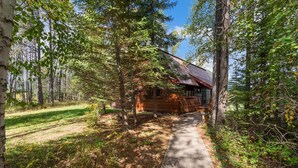 A cabin with a metal roof, surrounded by trees and a concrete path.