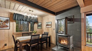 A wooden interior with a dining table, chairs, a fireplace, and framed pictures on the walls.