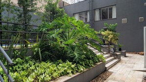 A modern building with a staircase leading to an upper level, surrounded by lush greenery and a stone-tiled patio.