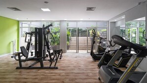 A gym with cardio machines, weight equipment, and large windows offering a view of greenery.