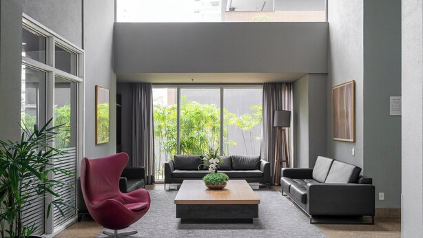 A modern living room with a large window, a red chair, a black sofa, and a coffee table with a plant.