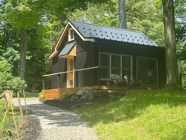 Een chalet met schuin dak, grote ramen en een veranda met stoelen.