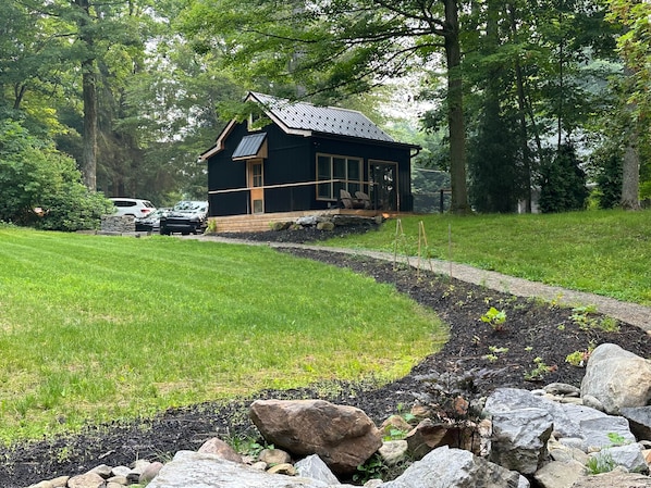 A cabin with a sloped roof, surrounded by a well-maintained lawn and a stone pathway leading to it. - Raven Cove - Tiny House with a Twist (Findley Lake)