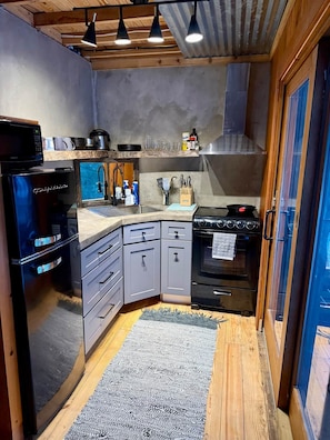 A compact kitchen with a built-in refrigerator, a stove, and a microwave. - Raven Cove - Tiny House with a Twist (Findley Lake)