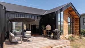 Una casa moderna con terraza de madera, mobiliario exterior y un ventanal grande con vistas al paisaje.