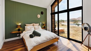 Un dormitorio moderno con una cama grande, suelo de madera, paneles de pared verdes y vistas al exterior.