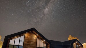 Una casa moderna con amplios ventanales y fachada de madera, bajo un cielo estrellado.