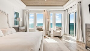 Ein geräumiges Schlafzimmer mit einem großen Bett, einer Sitzecke mit einem Sessel und Meerblick durch mehrere Fenster.