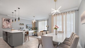 Une cuisine moderne dotée d’un îlot central, de luminaires suspendus et d’un coin repas avec une table et des chaises blanches.