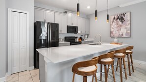 Une cuisine moderne avec des meubles blancs, un réfrigérateur noir, un four à micro-ondes et un grand îlot central doté de tabourets de bar.
