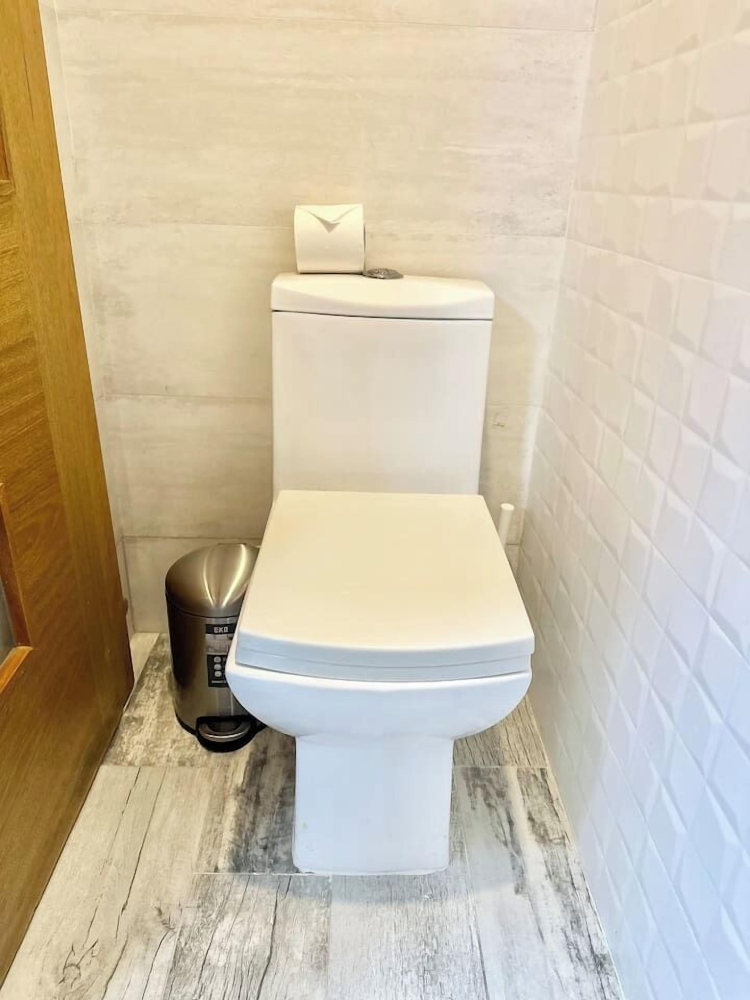 Un baño pequeño y funcional, con inodoro blanco, un cesto de basura y una puerta de madera.
