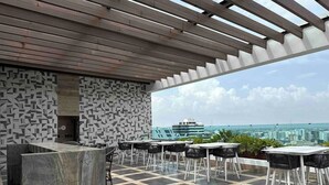 A rooftop terrace with a checkered floor, a bar area, and tables and chairs.