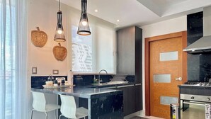 A modern kitchen with a central island, white bar stools, pendant lighting, and a built-in oven.