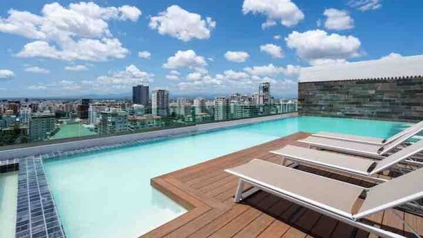 A rooftop pool with lounge chairs and a city view.