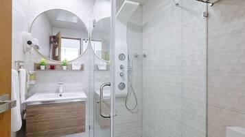 Un baño moderno con cabina de ducha de vidrio, tocador de madera, espejo redondo y una planta pequeña en el tocador.