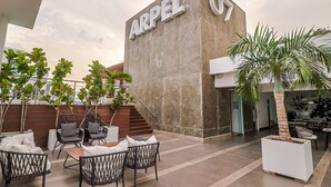 A modern hotel exterior with a prominent 'ARPEL 07' sign, outdoor seating area, and potted plants.
