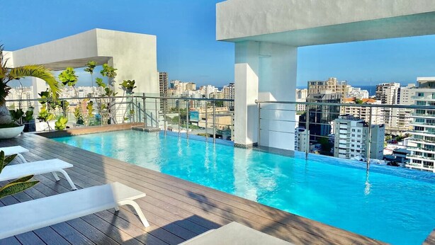 A rooftop pool with clear blue water, surrounded by wooden deck and lounge chairs.