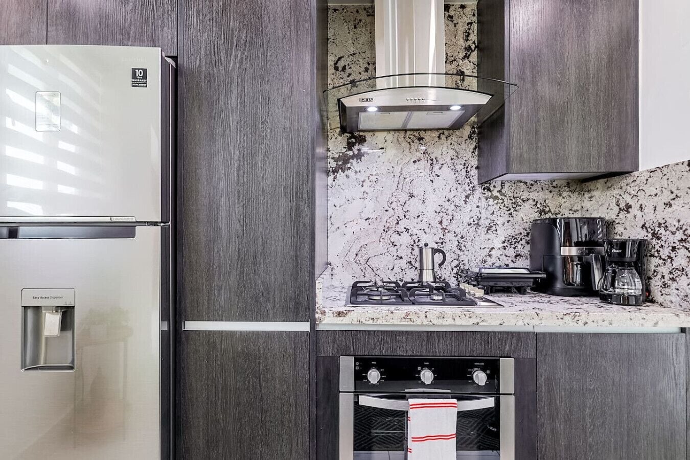 Een moderne keuken met een roestvrijstalen koelkast, een gasfornuis, een koffiezetapparaat en een inbouwoven.