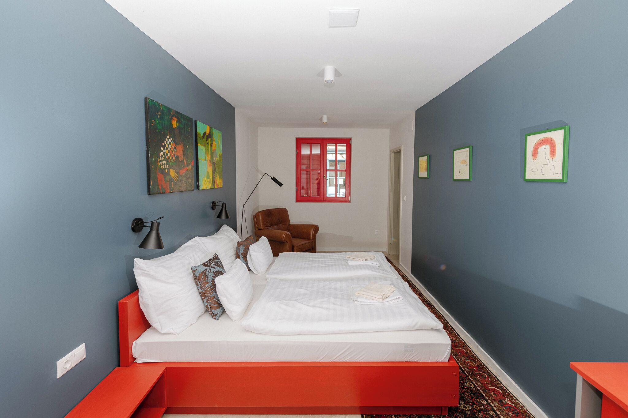 Un dormitorio con dos camas, una silla roja y obras de arte en las paredes.