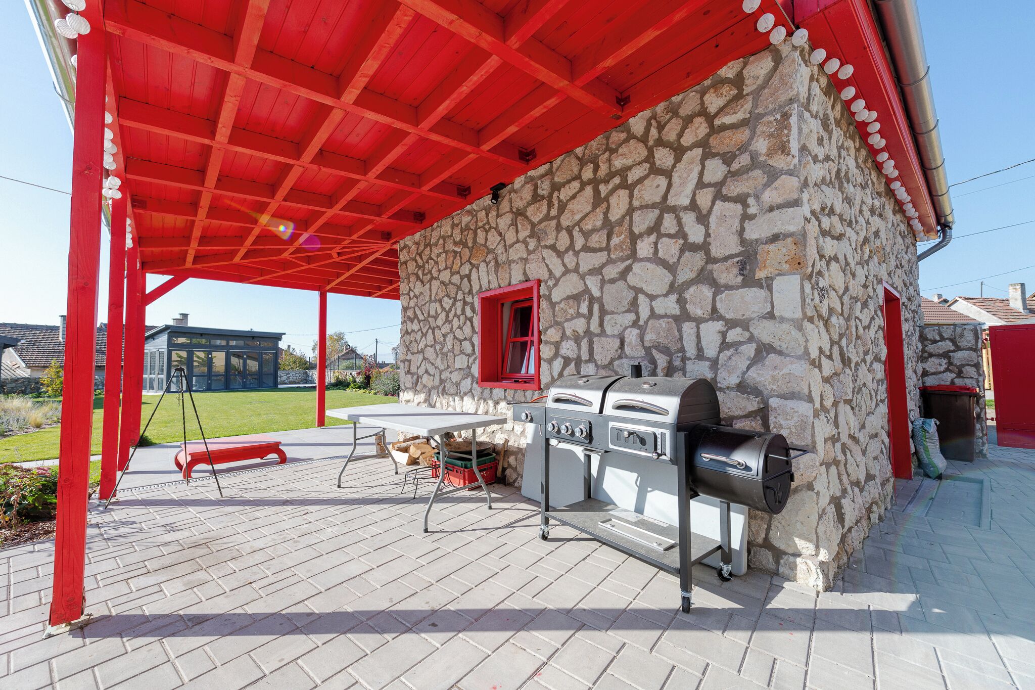 An outdoor patio with a stone wall, red roof, and barbecue grill.