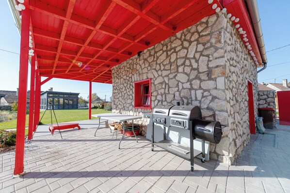 Un patio al aire libre con pared de piedra, techo rojo y una parrilla.