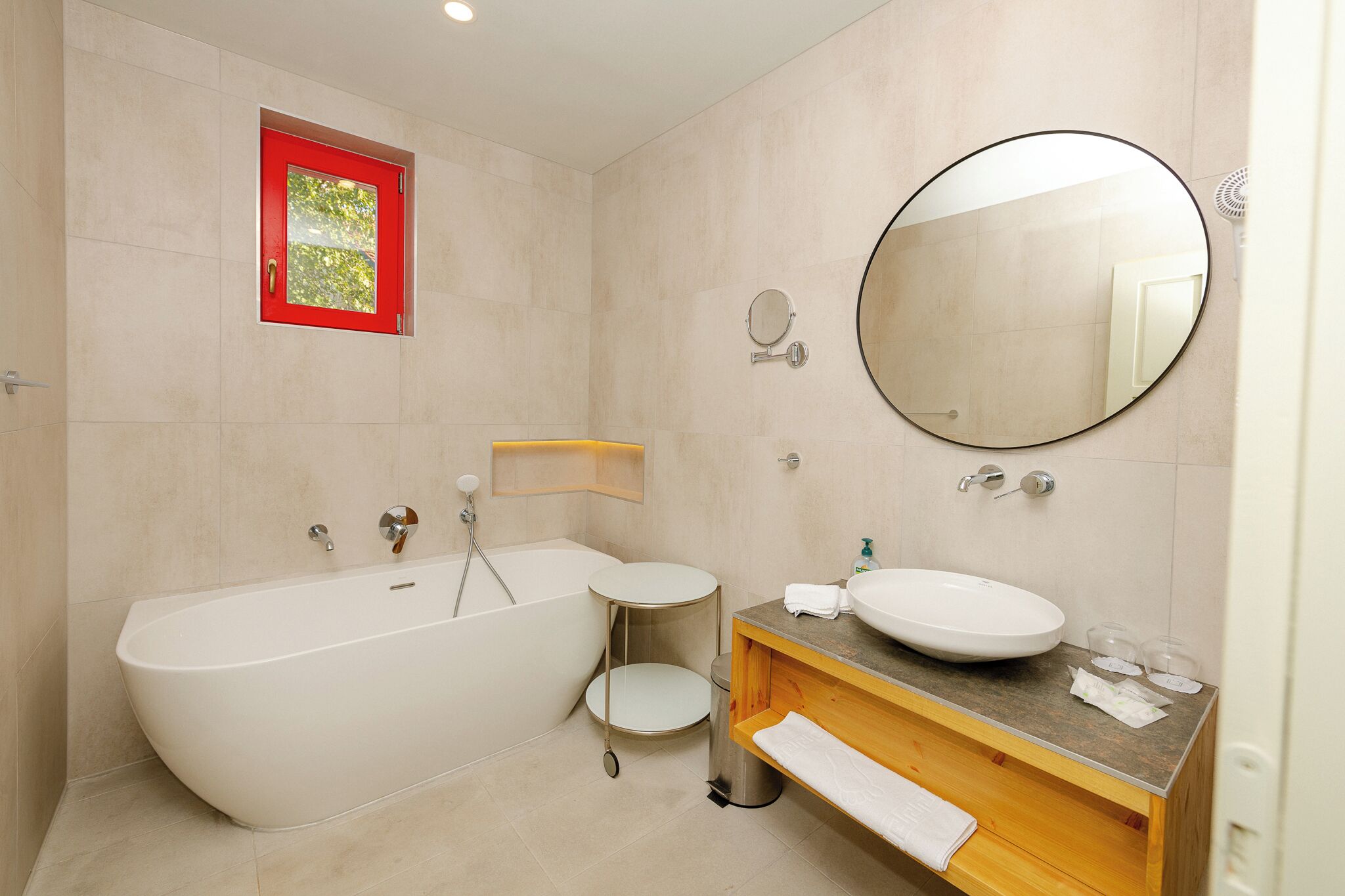 A modern bathroom with a freestanding bathtub, a round mirror, and a wooden vanity with a sink.