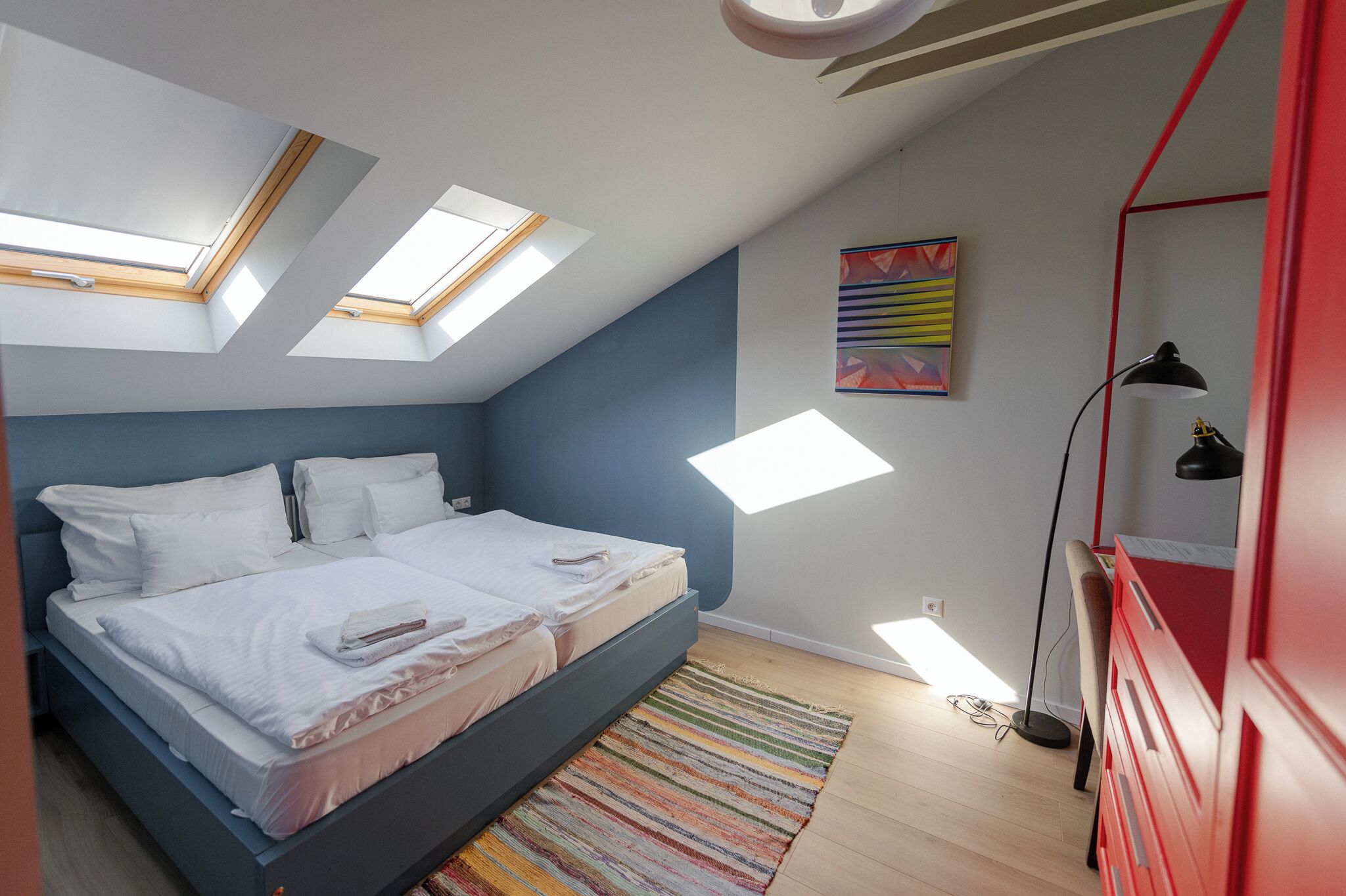 Un dormitorio con cama, tragaluces, un tapete colorido y un armario rojo.
