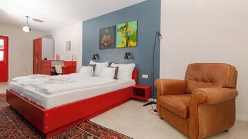A modern bedroom with a red bed, a brown leather chair, and abstract wall art.