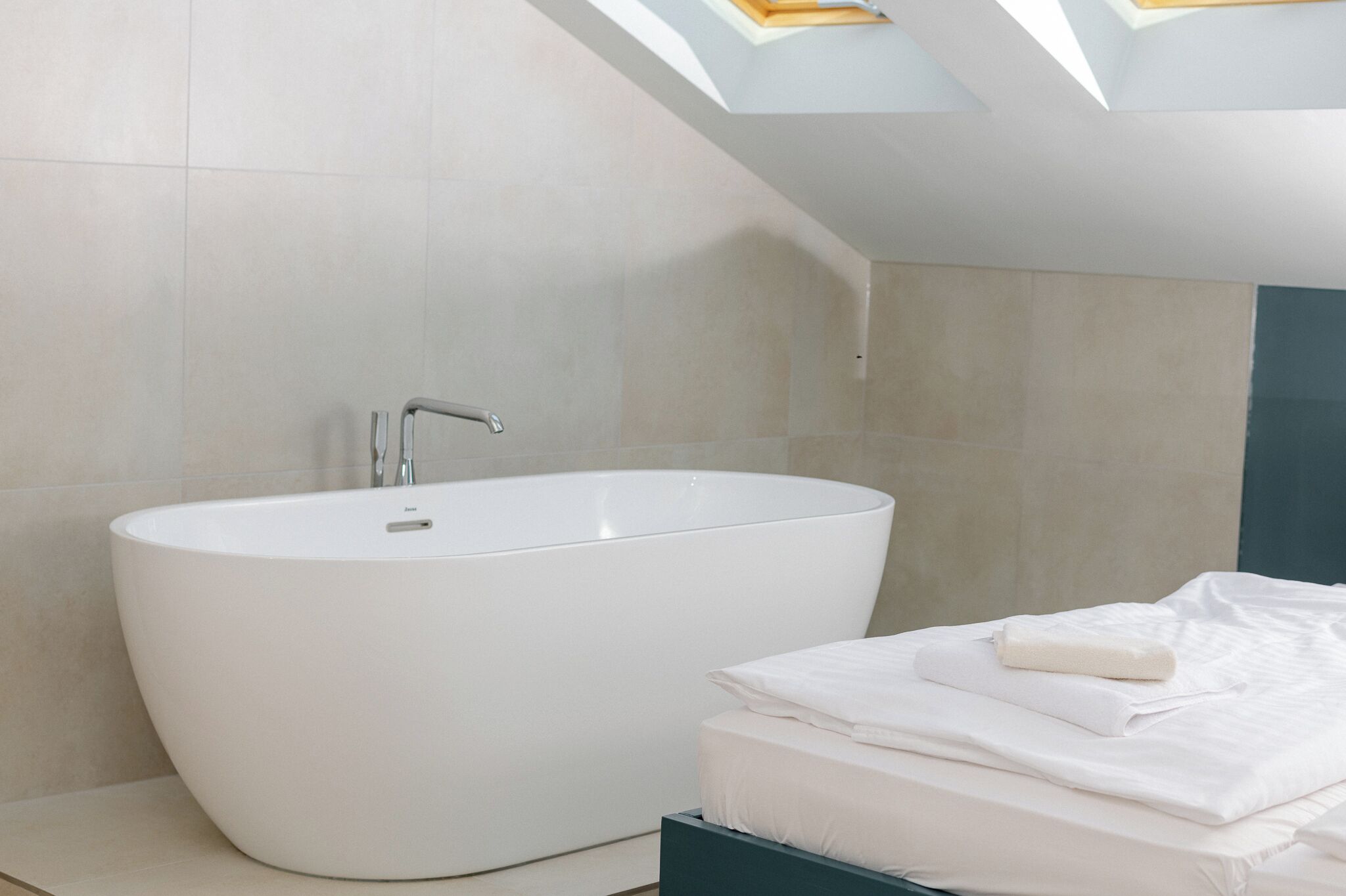Un baño moderno con una bañera independiente, ducha y una cama bien hecha con sábanas blancas.