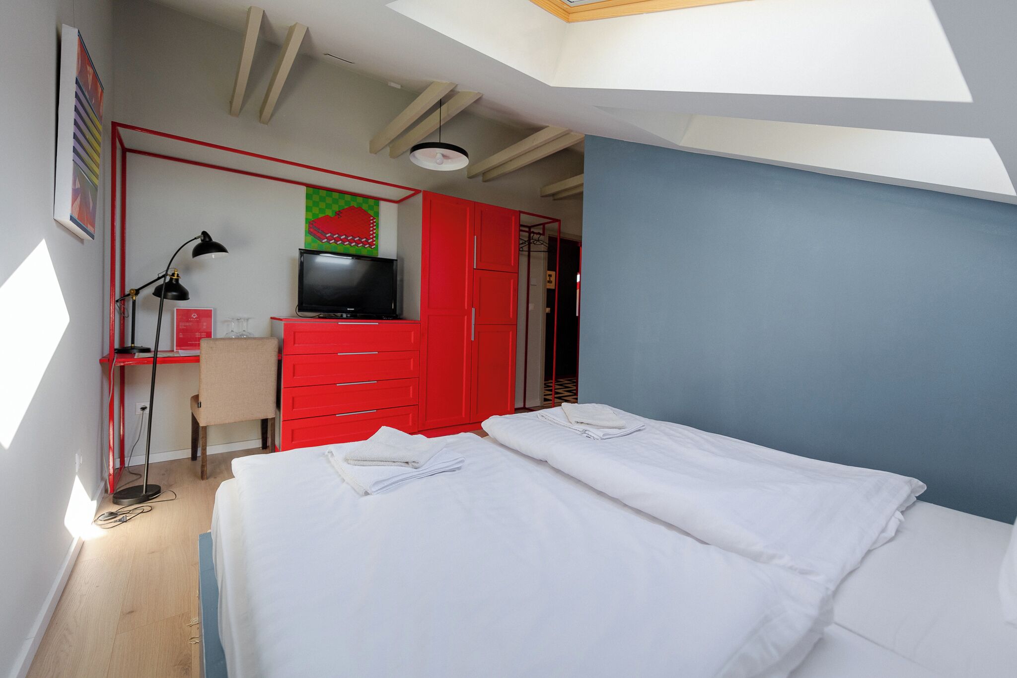 A bedroom with a bed, a desk with a TV, and red cabinets.